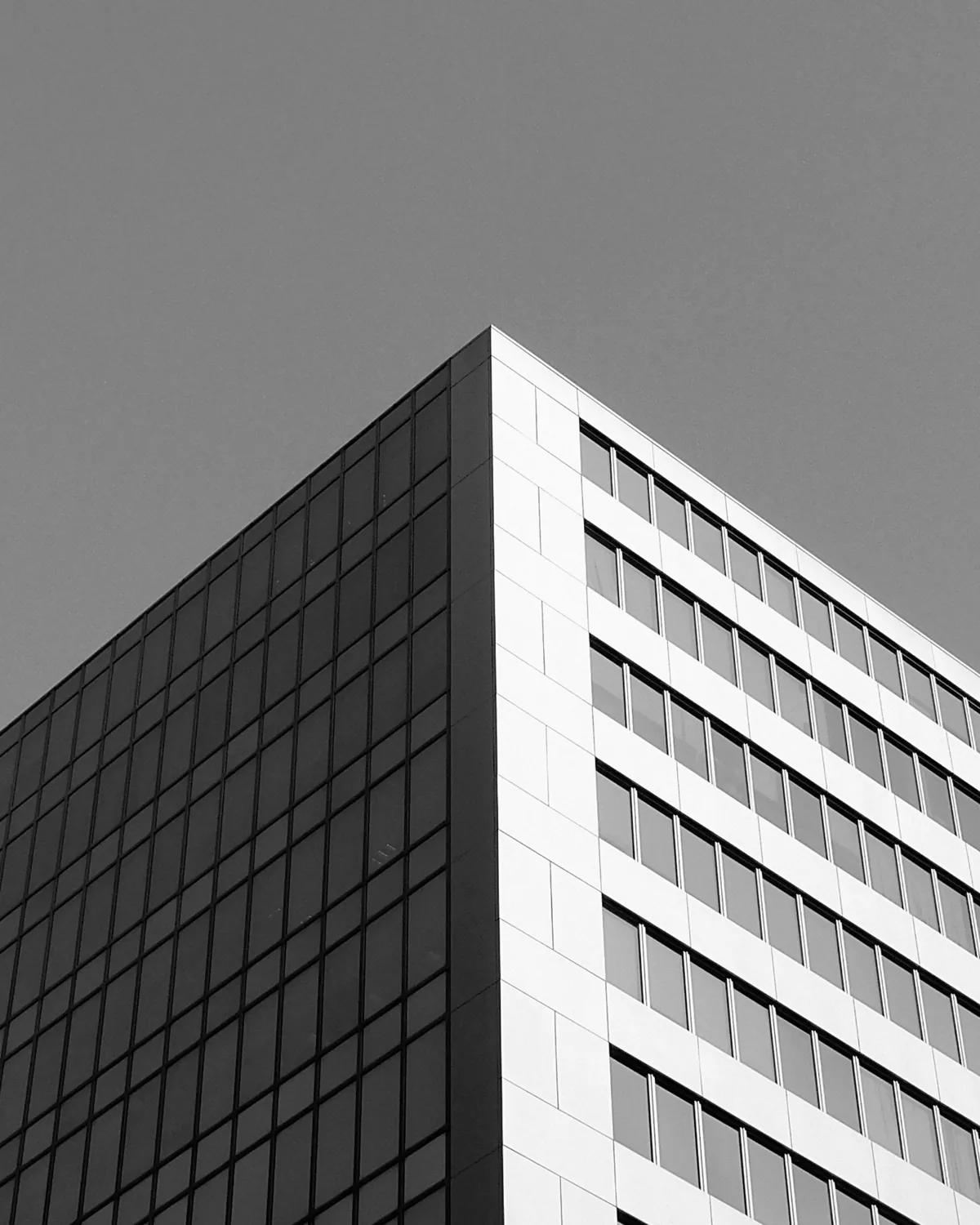 Glass and steel office tower seen from below against a pale sky
